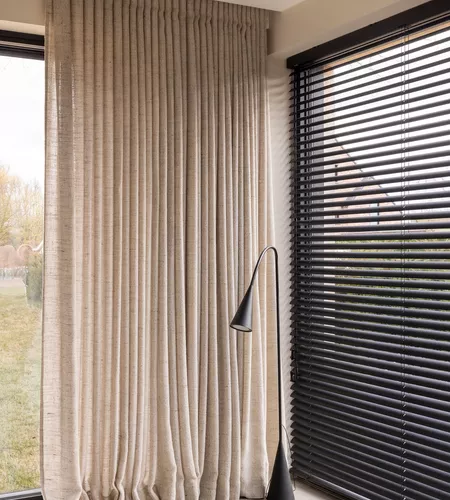 Zwarte aluminium lamellen in combinatie met beige schuifgordijnen in woonkamer in Marke geplaatst door Altex Raamdecoratie