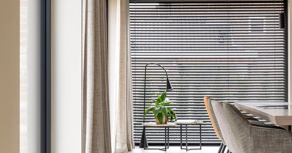 Zwarte aluminium lamellen in combinatie met beige schuifgordijnen in woonkamer in Marke geplaatst door Altex Raamdecoratie
