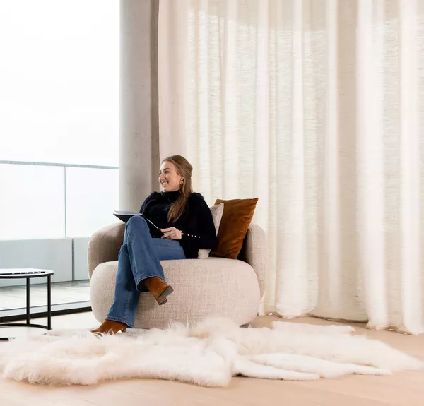 Tevreden vrouw die boek leest in zetel voor gordijnen