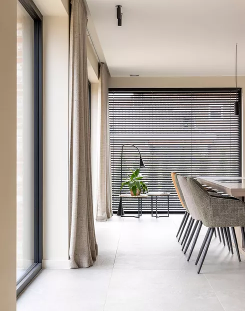 Zwarte aluminium lamellen in combinatie met beige schuifgordijnen in woonkamer in Marke geplaatst door Altex Raamdecoratie